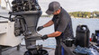 © Arttali_Neuro - Man in cap and gloves servicing a boat engine on the water, draining oil into a bucket. Marine maintenance, boat repair, engine service, waterside work, change oil