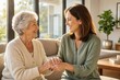 © saranya - Adult daughter gently holding her senior mother's hands in a sunlit living room, showing love, care, and family support.