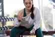 © Wavebreak Media - Woman sitting on padded bench in studio holding dumbbells by dumbbell rack wearing teal activewear