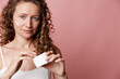 © SHOTPRIME STUDIO - Authentic middle aged woman applies moisturizer on her cheek, showcasing natural skin without retouching. Studio portrait against a pink backdrop, emphasizing skincare and care.