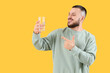 © Pixel-Shot - Young man pointing at glass of water on yellow background