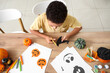 © Pixel-Shot - Teenage African-American boy cutting paper witch hat for Halloween decorations at home, top view