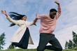 © Iryna - Joyful young couple jumping midair outdoors on a green hill with expansive sky for lifestyle poster background and active wellness campaign
