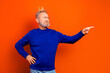© deagreez - Confident older man wearing a small crown and blue sweater pointing to the side against a bright orange background, playful portrait conveying pride, humor and leadership