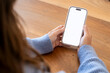 © simona - Person holding smartphone with blank white screen over wooden table, hands in blue sweater ready to use mobile phone