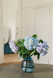 © Anna Sorokina/Stocksy - Blue hydrangea bouquet in glass vase on wooden table at home