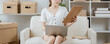 © Wicitr - A Young Woman Manages Her Small Business From Home: A focused young woman works on her laptop while holding a clipboard, surrounded by boxes in a home office.