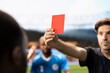 © DC Studio - Close-up shows a referee giving a red card to an angry player who complains about the dismissal, while teammates protest the controversial decision and rules violation during a dramatic soccer game.