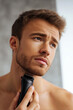 © Vitalii - Young man using a beard trimmer under his chin, suitable for shaving products and personal care