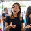 © Fahroni - Hispanic woman demonstrating strong leadership skills while coordinating charity fundraising event and giving clear directions to diverse volunteer group with colorful booths and banners