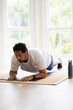 © wavebreak3 - Man performing forearm plank on mat at home in white tee, blue shorts, water bottle nearby
