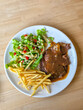 © CoreRock - Grilled steak with pepper sauce, golden french fry and fresh lettuce salad topped with diced tomato and creamy dressing, plated on white dish for hearty casual meal