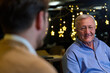 © .shock - Smiling Senior Man Conversing With Younger Relative In Cafe With Festive Christmas Lights