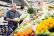 © caftor - Mature customer selects savoy cabbage with interest in grocery department of supermarket