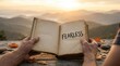 © tanin - Human hands holding an open book with fearless text, signifying courage and inspiration amidst a tranquil mountain sunrise