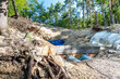 © sh99 - Eine tiefe Baugrube im Wald zeigt die Verlegung blauer Wasserrohre und Versorgungsleitungen durch eine Holzwand. Infrastrukturmaßnahme für die öffentliche Wasserversorgung in der Natur.