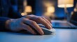 © Lamduan - Hand resting on a white computer mouse during digital tasks at a desk with a laptop and blue ambient lighting.