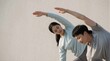© honigjp31 - A young Asian couple practicing yoga and stretching exercises together outdoors against a minimalist neutral wall.