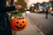 © Hisham Abrar - Child holding orange pumpkin trick or treat pail filled with candy on neighborhood street at twilight, jack o lantern