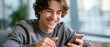 © Atchariya63 - Smiling young man using smartphone in modern office, relaxed casual portrait with natural light