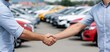 © ckybe - Successful car sale handshake between dealer and customer outdoors with multiple cars in daylight.