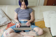 © Eliza da Rosa/Stocksy - Young adult working in their laptop at their couch in the morning