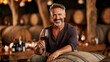 © Oleg - Man holding wine glass smiles while sitting on a barrel in a winery during evening