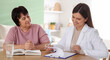 © New Africa - Caregiver with clipboard talking to senior woman at wooden table indoors