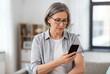 © Meow Creations - Older woman with grey hair looking at her smartphone while wearing a glucose monitor on her arm