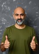 © Maryna - Bald middle aged man with grey beard wears green t shirt. Cheerful person gives thumbs up gesture against textured dark background. Friendly male model smiles looking at camera. Confident guy shows