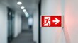© BZXO - Modern building hallway featuring an illuminated red emergency exit sign with right arrow and running man icon for safety compliance.