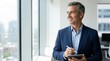 © FryArt - Confident businessman looking out office window holding tablet