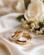 © Wendy - Two polished gold wedding rings arranged on soft ivory satin beside delicate flowers, photographed in close focus with a dreamy romantic background.