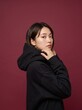 © Luthfi - Young Asian Woman in Stylish Black Cotton Hoodie Posing Against a Deep Red Studio Background