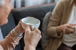 © 220 Selfmade studio - Senior woman cup tea home sofa Senior woman holding ceramic cup during relaxed tea time at home on sofa with another person in soft focus, warm indoor lifestyle scene