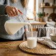 © Rizwan Akbar - Person wearing sweater pouring fresh milk into ribbed glass on wooden dining table in bright warm kitchen setting.