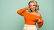 © Yassine - Beautiful blonde woman wearing an orange off shoulder sweater smiling and pointing at her chest while posing against green background
