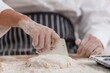 © BESTIMAGE - Close up hands of baker cutting fresh dough with plastic dough scraper on flour covered table Chef hands using bench scraper tool to portion dough while making homemade bread in bakery