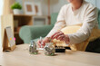 © Joi_studio - Person putting coin into savings jar with cash and calculator at home, saving money, household budgeting, financial planning and future financial goals
