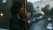 © Yulia Skletinski  - Thoughtful young woman holding warm cup beside rain streaked window, gazing outside in quiet evening light with soft reflections, blurred city glow, cozy indoor mood and calm contemplative atmosphere