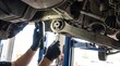 © Nazlykhan - Auto mechanic repairing vehicle suspension underneath a raised car with wrench and inspection lamp. Automotive maintenance, repair service, workshop safety and professional technician concept.