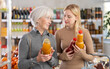 © JackF - Girl with senior female woman pick up juice in store. Customer consider and make choice between tomato and peach juice, compare varieties products. Client hesitate before buying, choose fruit juice