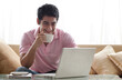 © IndiaPix - Smiling young man using laptop while having a cup of coffee