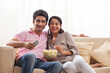 © IndiaPix - Smiling young couple watching TV while eating popcorn