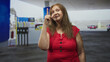 © Krakenimages.com - Woman points index finger up at a gas pump under canopy in a building, wearing red blouse and smiling, senior hispanic facing camera; assertive warning.
