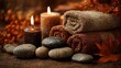 © Harry - Rolled soft brown bath towels stacked with smooth zen stones and glowing pillar candles for relaxing autumn spa session atmosphere