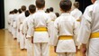 © PAVEL - A group of children wearing white karate uniforms and yellow belts standing in a line during a martial arts class.