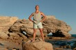 © Andrii Zastrozhnov - Fit man standing atop a coastal rock formation for fitness and travel banner background with adventurous lifestyle mood