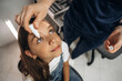© standret - Young girl receiving eye drop treatment from adult caregiver in a clinical setting with medical equipment and bright lighting visible in the background