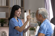 © Ratirat - Young asian female caregiver feeding senior elderly man patient at home. Compassionate nurse serving food with smile expressing care support and warmth inside comfortable domestic room